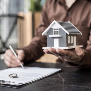 A person reviewing a contract while holding a miniature house model